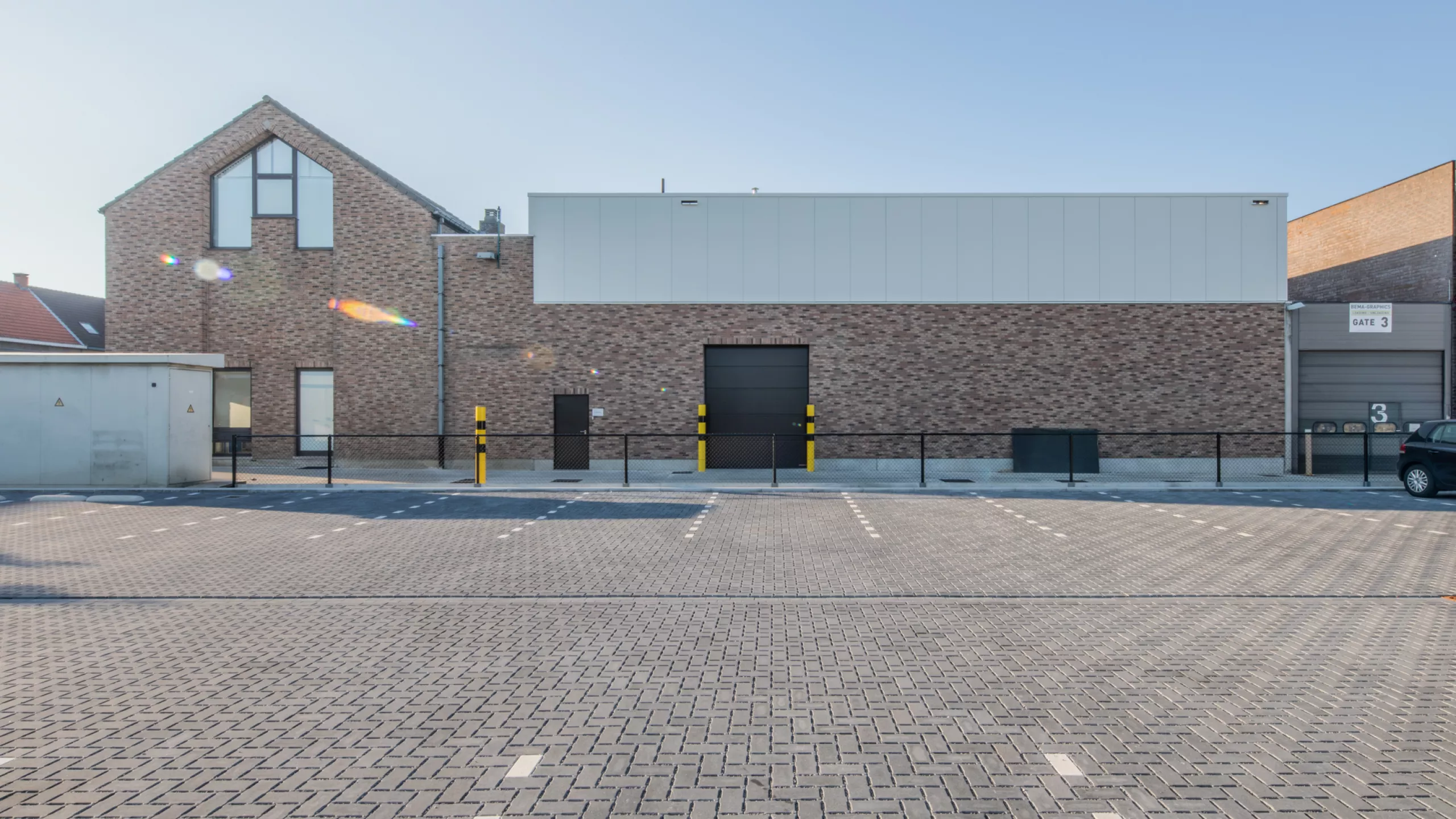 Afbraak bestaand magazijn + nieuwbouw Nauta Holding. De afbeelding is een vooraanzicht van de nieuwbouw. Het magazijn bestaat uit rode steen en grijze wanden. Het bevat een zwarte poort en deur.