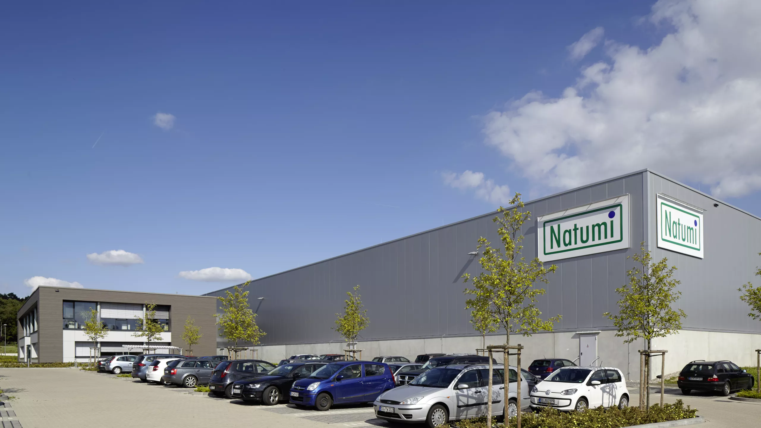 Productiegebouw inclusief kantoren en opslagruimte Natumi Duitsland. Het gebouw is opgebouwd met beton. Bovenaan in de rechterhoek hangt het logo van Natumi.