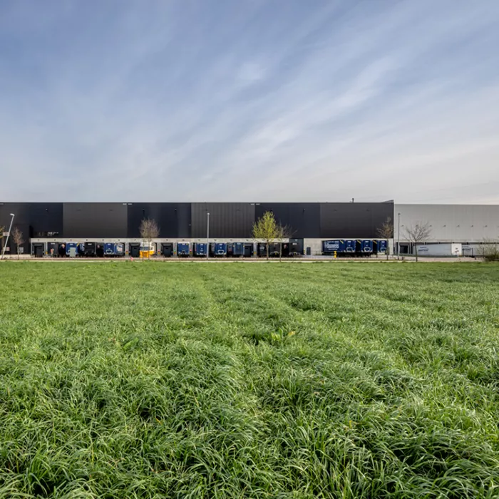 Vooraanzicht opslagmagazijn en kantoor Bauwens Logistics. De afbeelding is gemaakt vanuit het grasveld tegenover het bedrijf. Het gebouw is gebouwd met staal.