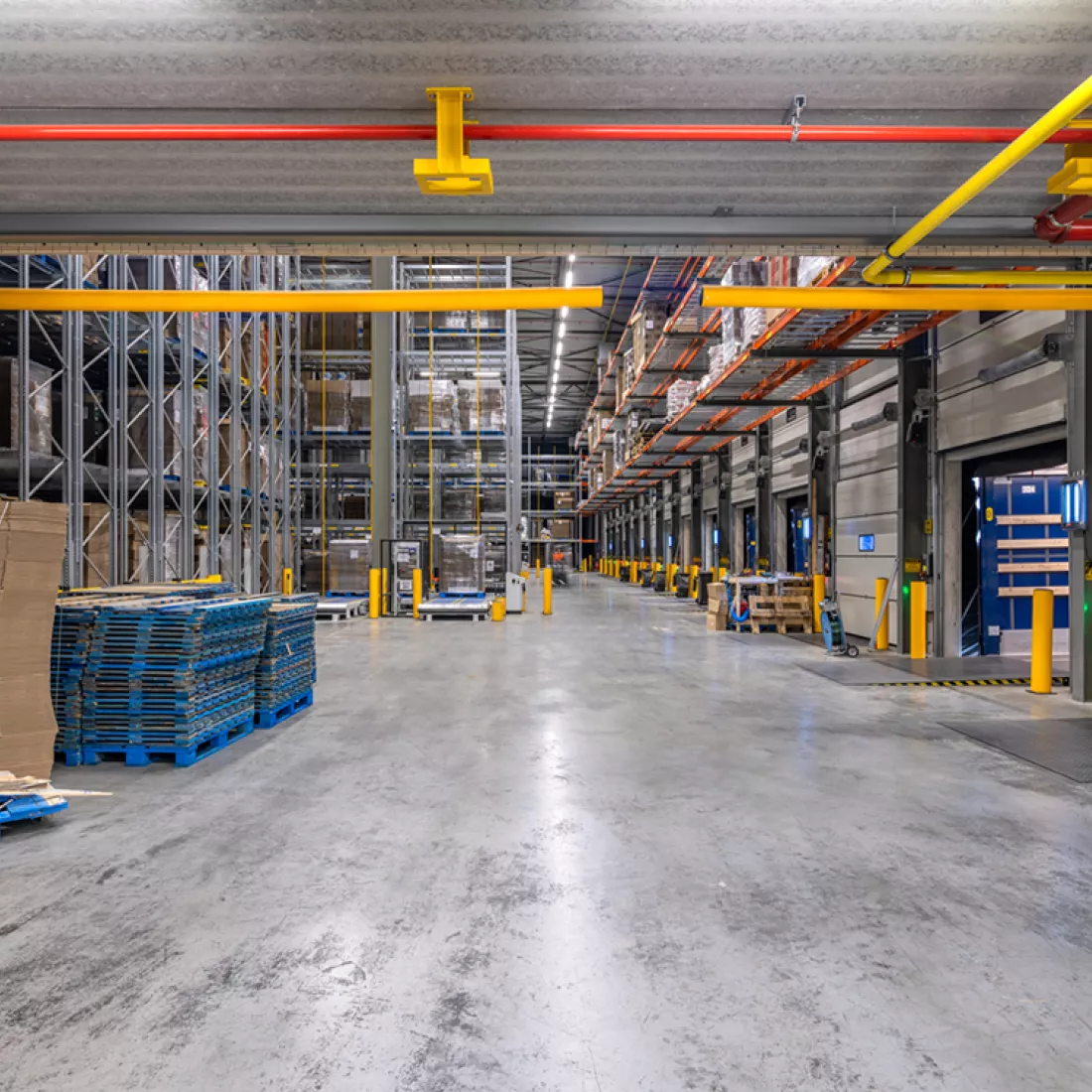 Vooraanzicht binnenkant opslagmagazijn Bauwens Logistics. Er zijn allemaal rijen met rekken waar materiaal opgeslagen is.