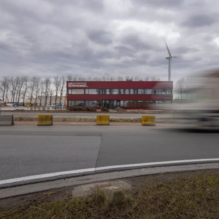 Vooraanzicht bedrijfspand Terberg Gent. Het gebouw is rood en heeft twee verdiepen. Zowel de onderste als bovenste verdieping bestaat uit grote ramen met zwarte omkadering. Bovenaan links hangt het logo van Terberg. Het gebouw is gebouwd uit staal.