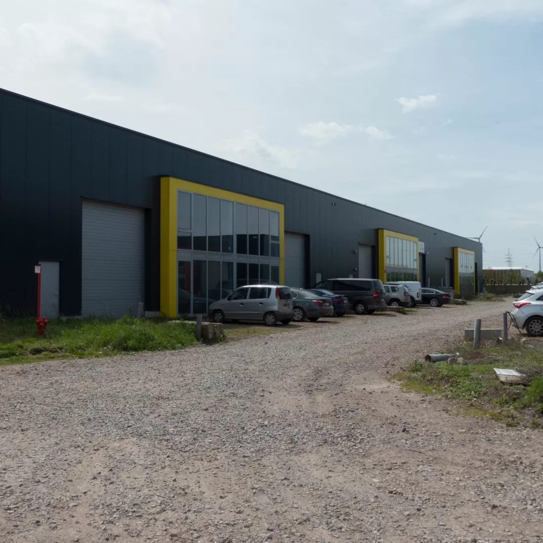 KMO Units Picolo - Van Ende: geel. De units zijn opgebouwd met een combinatie van verschillende materialen. De units bestaan uit zwarte platen, grijze poorten en deuren. Er is een deel van het gebouw dat iets meer naar voor komt. Het bestaat volledig uit ramen en heeft een gele omranding.