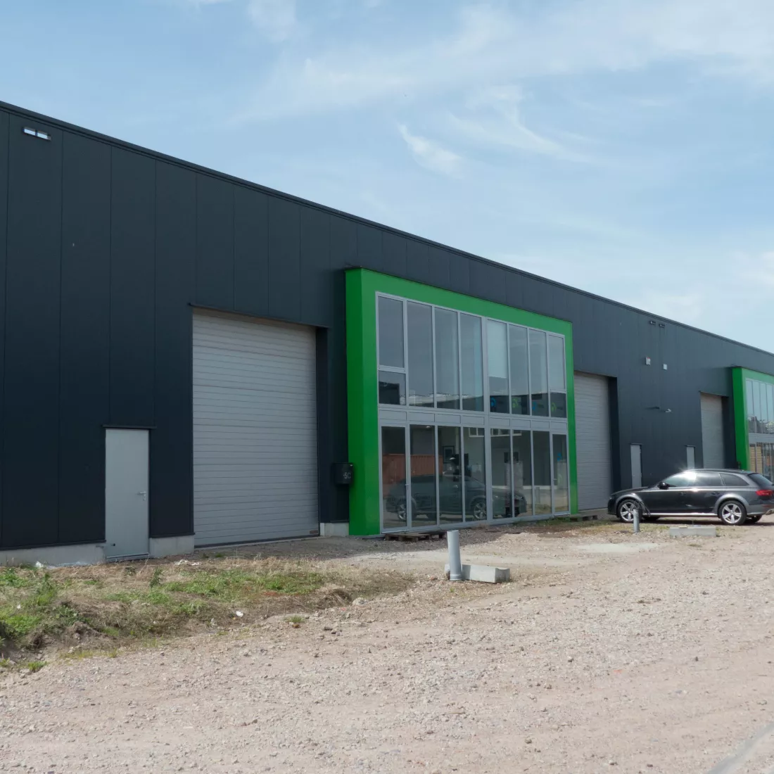KMO Units Picolo - Van Ende: groen. De units zijn opgebouwd met een combinatie van verschillende materialen. De units bestaan uit zwarte platen, grijze poorten en deuren. Er is een deel van het gebouw dat iets meer naar voor komt. Het bestaat volledig uit ramen en heeft een groene omranding.