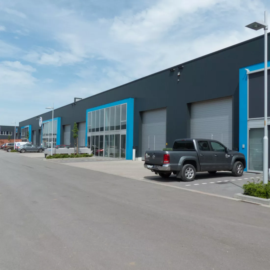KMO Units Picolo - Van Ende: blauw. De units zijn opgebouwd met een combinatie van verschillende materialen. De units bestaan uit zwarte platen, grijze poorten en deuren. Er is een deel van het gebouw dat iets meer naar voor komt. Het bestaat volledig uit ramen en heeft een blauwe omranding. Voor de units zijn er parkeerplaatsen voorzien.