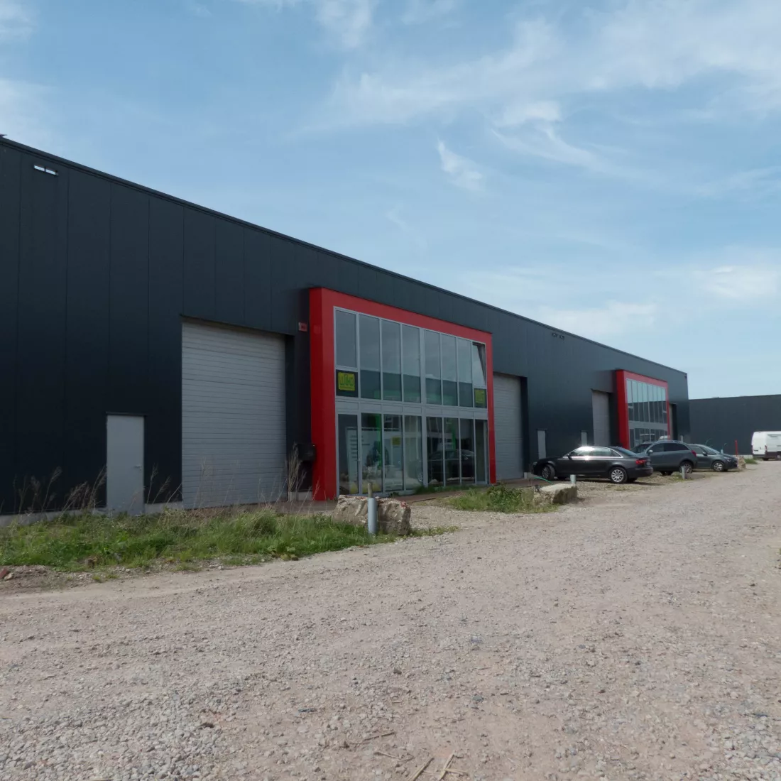 KMO Units Picolo - Van Ende: rood. De units zijn opgebouwd met een combinatie van verschillende materialen. De units bestaan uit zwarte platen, grijze poorten en deuren. Er is een deel van het gebouw dat iets meer naar voor komt. Het bestaat volledig uit ramen en heeft een rode omranding.