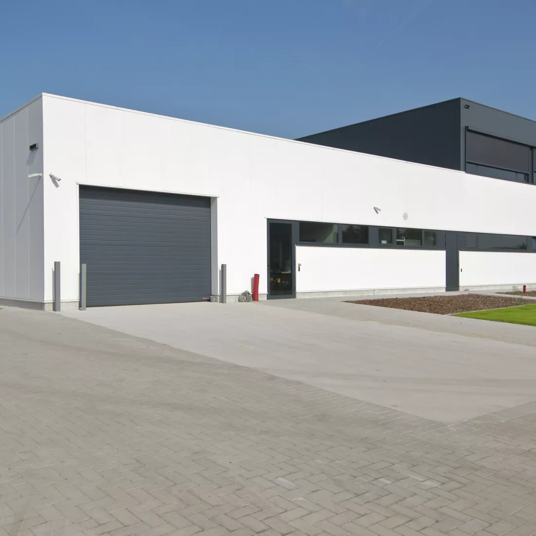Zijaanzicht productiehal en kantoor Argina. Het gebouw is wit met zwart. Tijdens de opbouw is staal gebruikt.