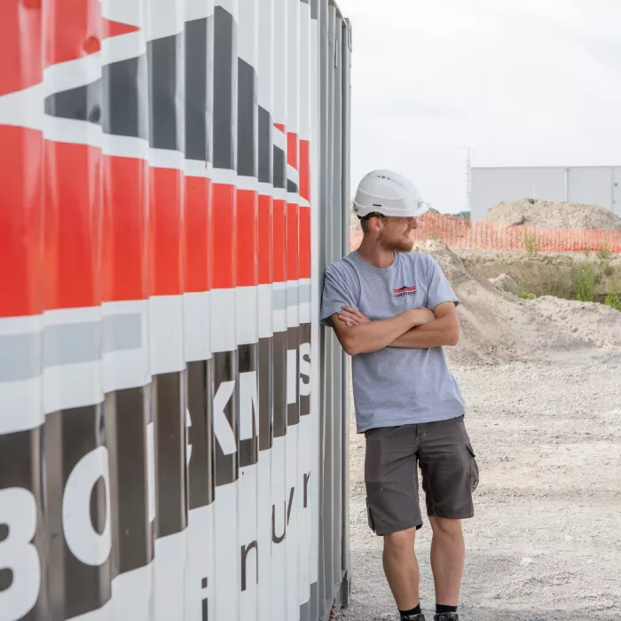 Een mederwerker op bouwterrein die tegen een Bolckmans container leunt