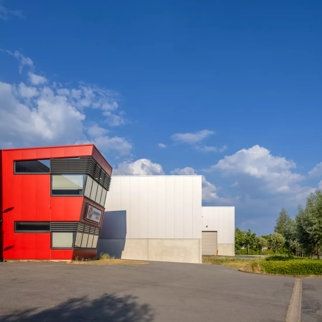Achterkant magazijn Foriver. Het gebouw is grijs en gemaakt uit staal. Achter het gebouw staat een rood kantoor.