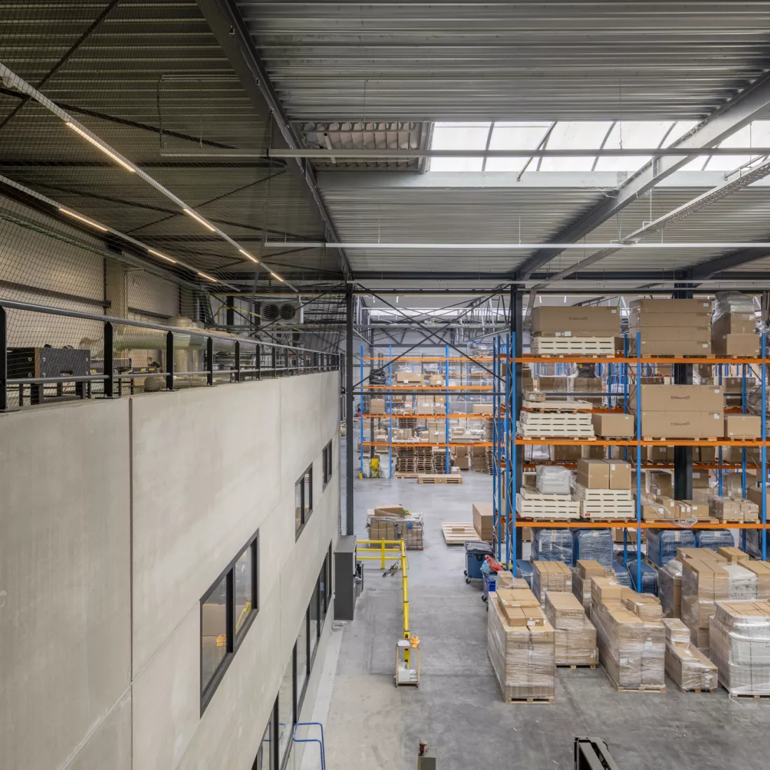 Bovenaanzicht Ethnicraft - Magazijn. Rechts bevindt zich het magazijn. In het magazijn staan blauwe met oranje rekken met producten er in opgeslagen. Links bevinden zich drie verdiepingen. De bovenste verdieping is een ontspanningsruimte.