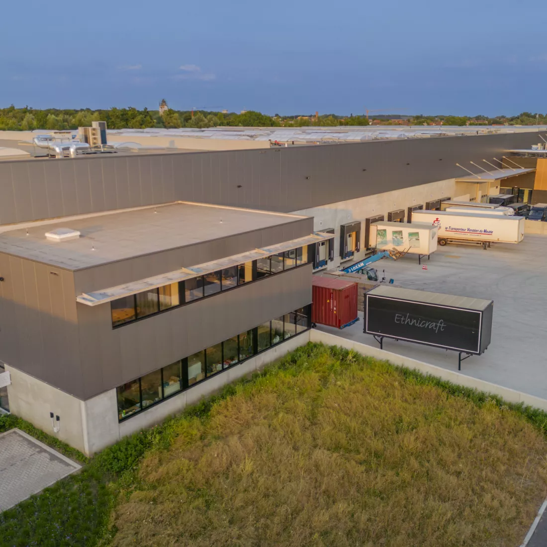 Ethnicraft droneshot. Het gebouw bevindt zich op deze afbeelding links. Het gebouw heeft een betonlook en bestaat uit grijze platen. In het midden bevindt zich het dock. 