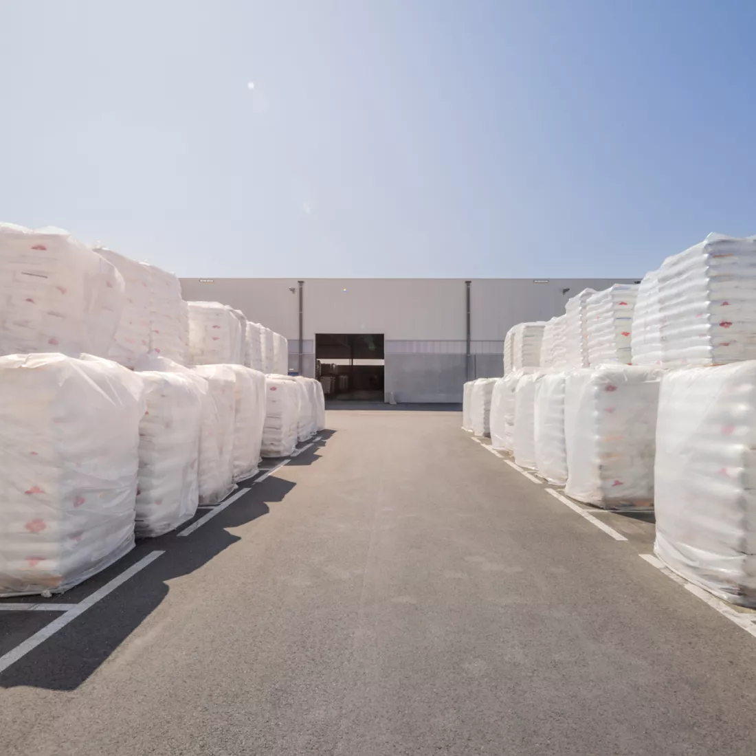 Vooraanzicht magazijn - Karl Schmidt. Voor het magazijn liggen producten opgeslagen in witte afgebakende vakken. Het magazijn bestaat uit beton en staal.