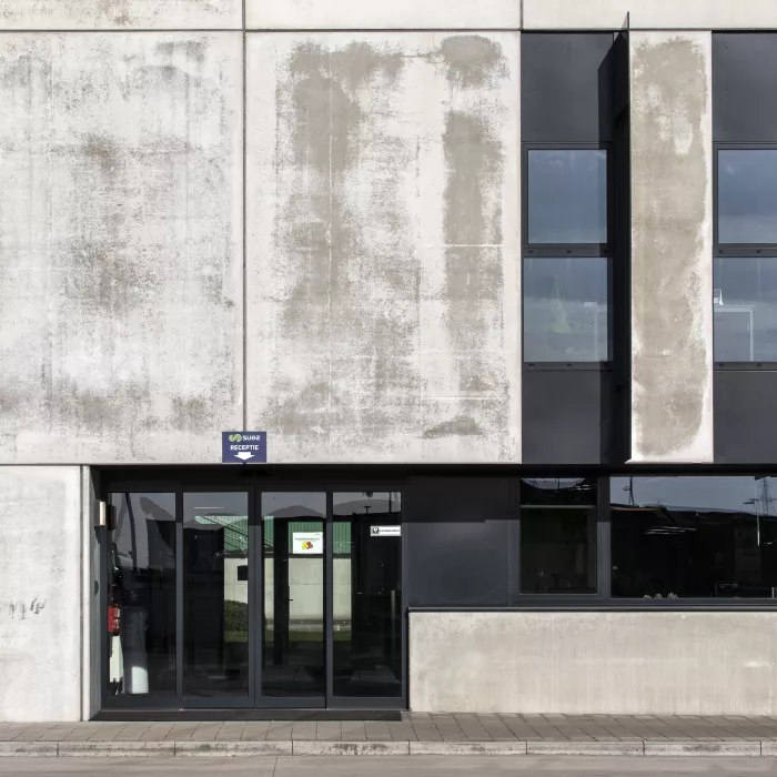 Inkom sorteer- en recyclagecentrum - Sita kantoor & garage. De inkom bestaat uit een glazen schuifdeur met zwarte omranding. rechts bevinden zich ramen met zwarte omranding.