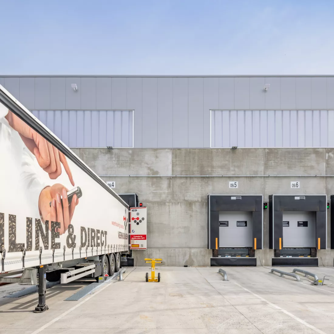 Close-up dock - Verkooijen. De poorten zijn wit en hebben ene zwarte omranding. Het dock bestaat uit beton. Links is er een vrachtwagen aan het laden of lossen.