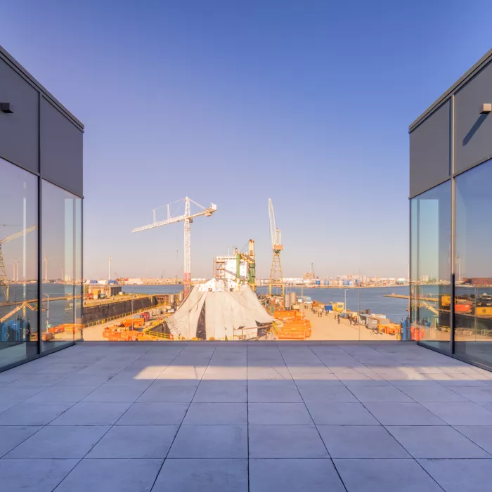 Bovenste verdieping kantoor EDR. De afbeelding is gemaakt vanop een balkon op de bovenste verdieping van het kantoor. Zowel rechts als links van het balkon bevindt zich nog een deel van het kantoor. Vanaf het balkon heb je uitzicht over de haven van Antwerpen.