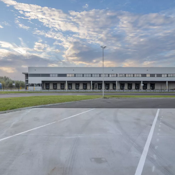 Vooraanzicht sorteercentrum Weerts Evergem (Post NL). Onderaan bevinden zich zwarte poorten van het dock voor het laden en lossen van vrachtwagens. Bovenaan bevinden zich kleine ramen.