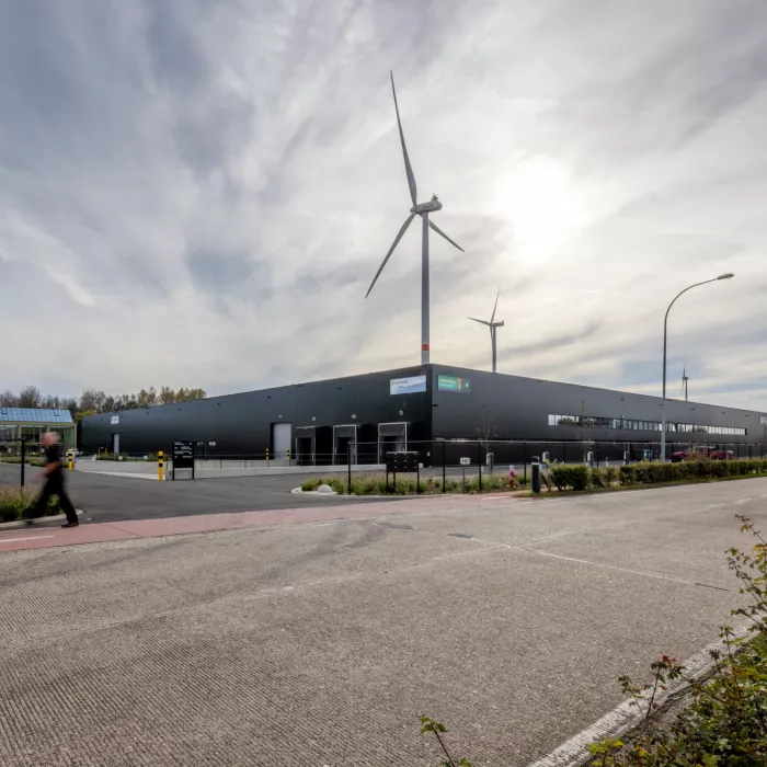 Zijaanzicht zwart magazijn Immo Bolckmans - Proost met dockbeheer. Dit voor het laden en lossen van vrachtwagens. In de achtergrond staan twee witte windmolens. De foto is gemaakt aan de overkant van de straat.