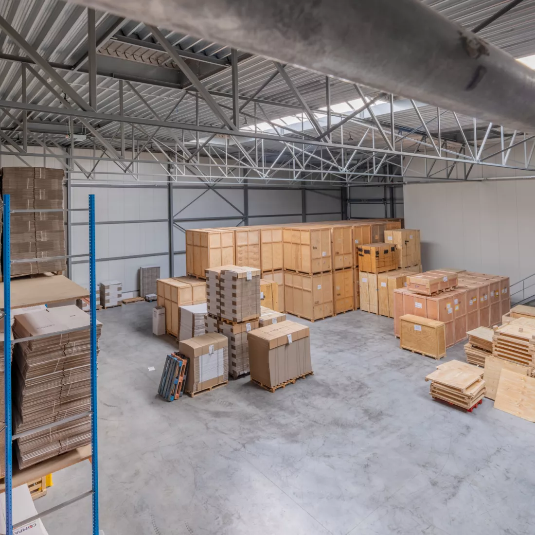 Bovenaanzicht van het magazijn van Putters-Move Relocation gemaakt uit staal. Magazijn van Putters-Move. Er staan allemaal houten kisten op elkaar gestapeld. Ook liggen er kartonnen dozen in het magazijn.