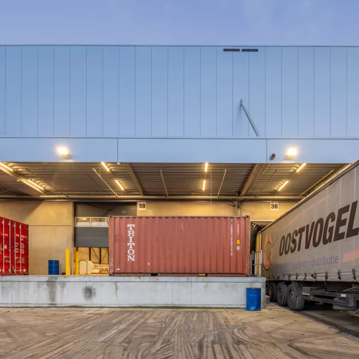 Close-up van het dock voor het laden en lossen van vrachtwagens. Er staan rode containers voor het dock. Links staat een vrachtwagen van Oostvogels.