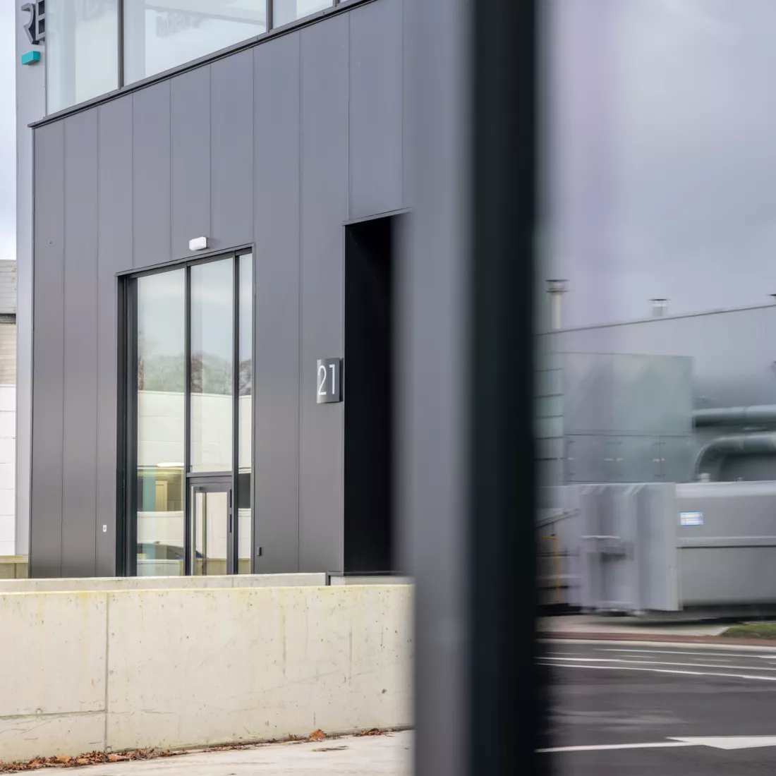 Close-up industrieel gebouw Reynders Pharma. De inkom bestaat uit een glazendeur met een omranding van ramen.