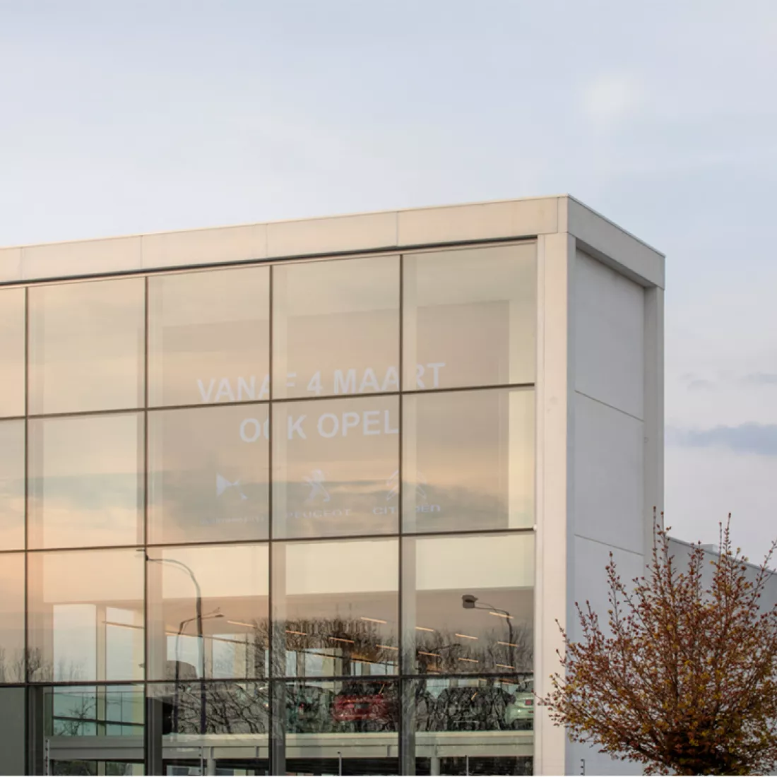 Garage Van Hoecke glaspartij. Door de ramen kan je een LED-screen zien. Hierop staat "Vanaf 4 maart ook Opel" met daaronder logo's van automerken. Onder het bord zijn twee verdiepen waar auto's tentoongesteld staan.