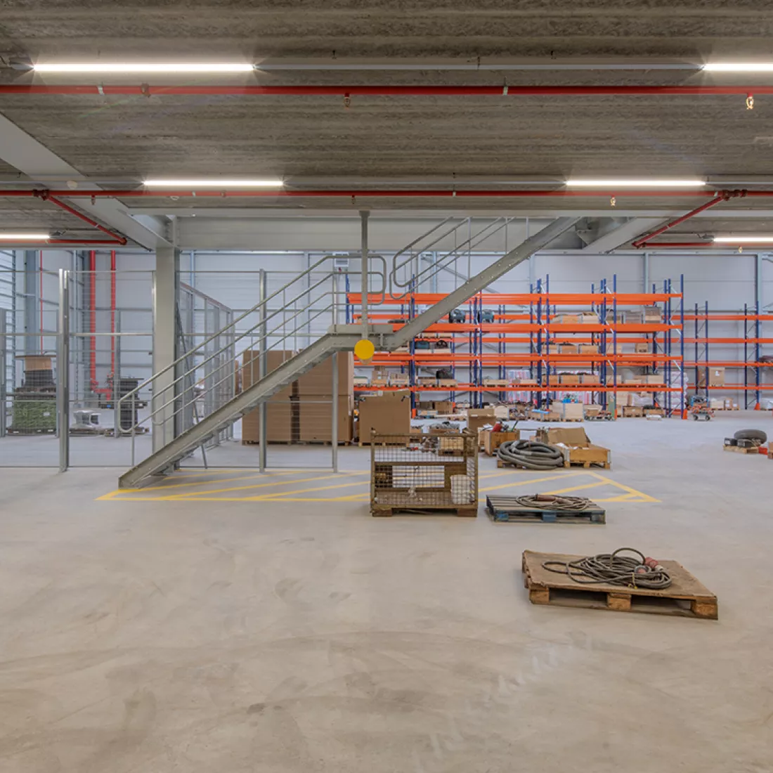 Binnenkant Add logstieke hal en workshop C. De afbeelding is vanaf de gelijkvloers gemaakt. In het midden staat er een trap om naar de eerste verdieping te gaan. Achteraan bevinden zich rekken.