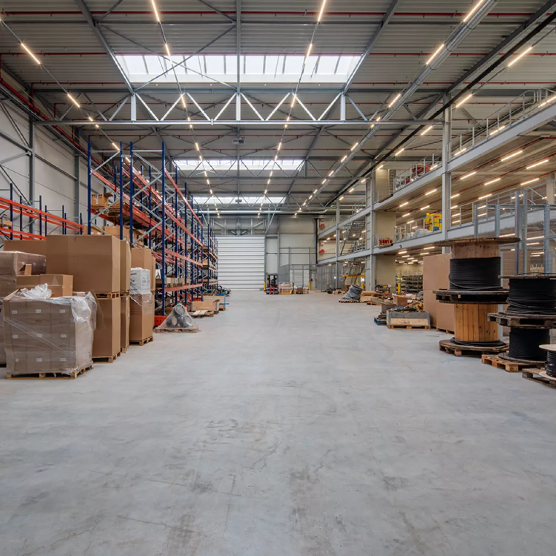 Binnenkant logistieke hal en workshop C. Rechts bestaat de loods uit drie verdiepen. Links staan rekken. Achteraan bevindt zich een poort. Bij de opbouw is er staal gebruikt.
