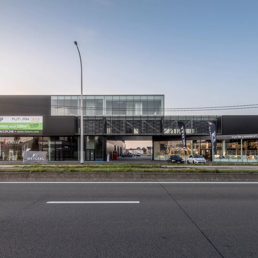 Vooraanzicht bedrijfsunits Futurn. Het gebouw heeft drie verdiepen. Het is gemaakt uit staal. De foto is gemaakt vanaf de overkant van de straat. Op de gelijkvloers is een doorgang om naar de parking te gaan.