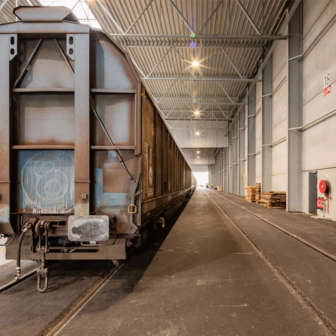 Binnenkant staalplaten magazijn + uitbreiding terminal Zuidnatie Kaai 472. Er zijn sporen en links staat een transporttrein. Het plafond bevat een lichtstraat.