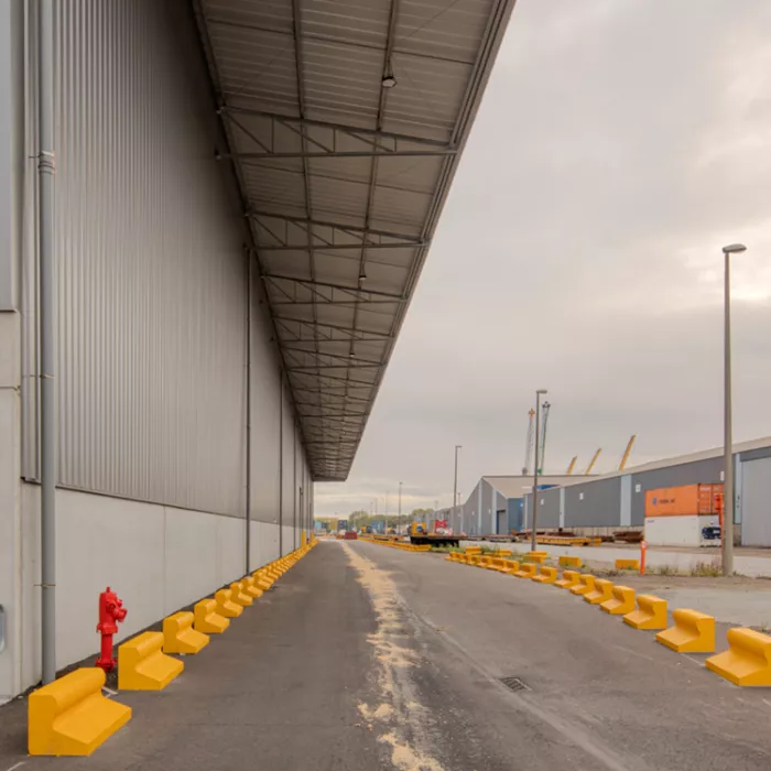 Zijaanzicht staalplaten magazijn + uitbreiding terminal Zuidnatie Kaai 472. Links bevindt zich het grijze magazijn. Rechts een weg afgebakend met gele betonnen stenen.