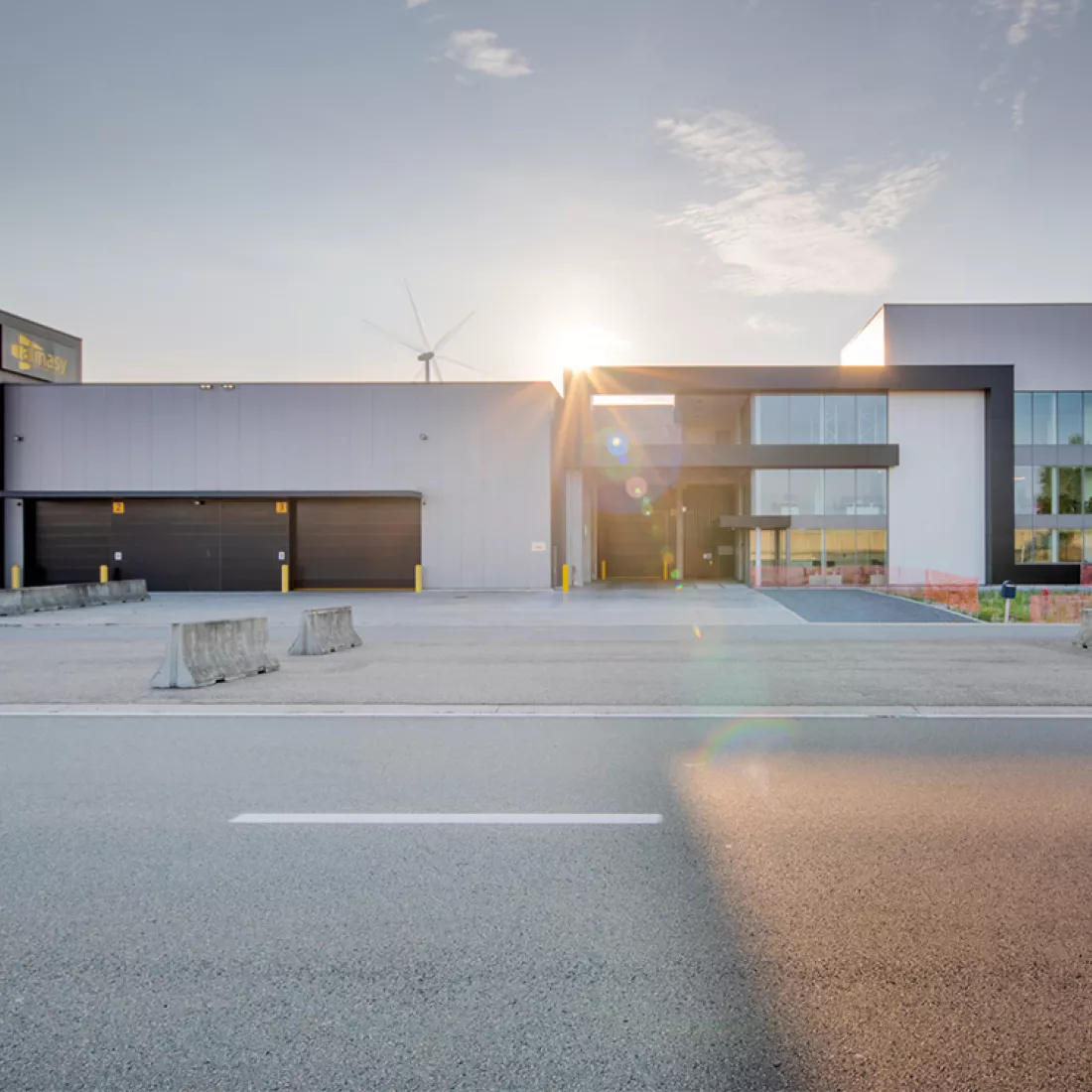 Vooraanzicht Almasy kantoor. Rechts bevindt zich het kantoor en links het bestaande industriegebouw. Het gebouw bestaat uit grijze en zwarte platen. Het kantoor bevat veel ramen en bestaat uit drie verdiepingen. Bij de opbouw werd een combinatie van materialen gebruikt.