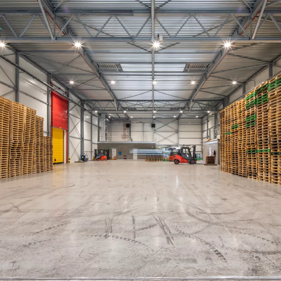 Binnenkant diepvriesloods Citrosuco. Links en rechts staan paletten opgeslagen. Achteraan zie je heftrucks. De loods is gebouwd met staal.