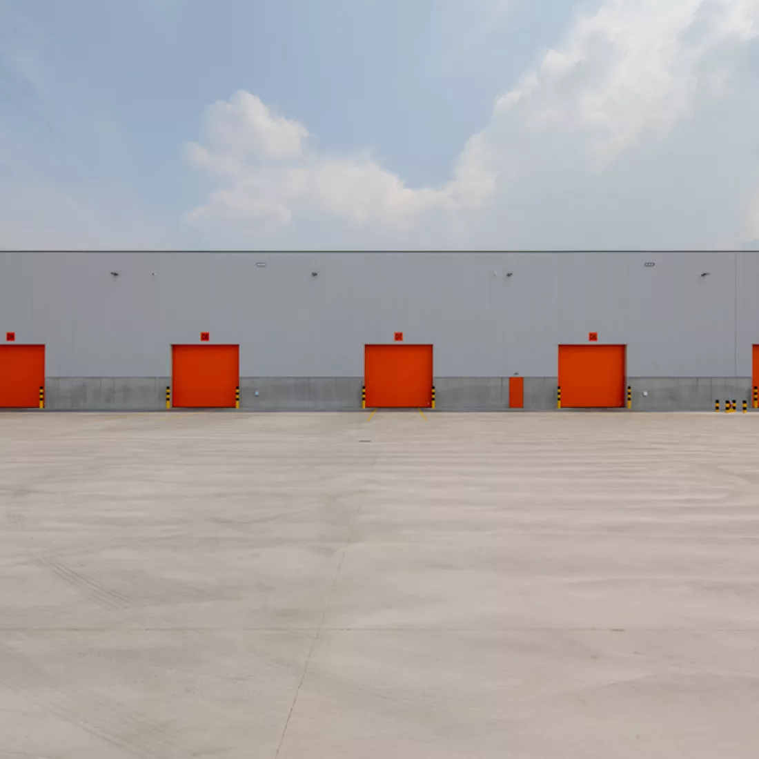 Vooraanzicht magazijn Promat hal 9. Het gebouw is grijs en heeft oranje poorten.