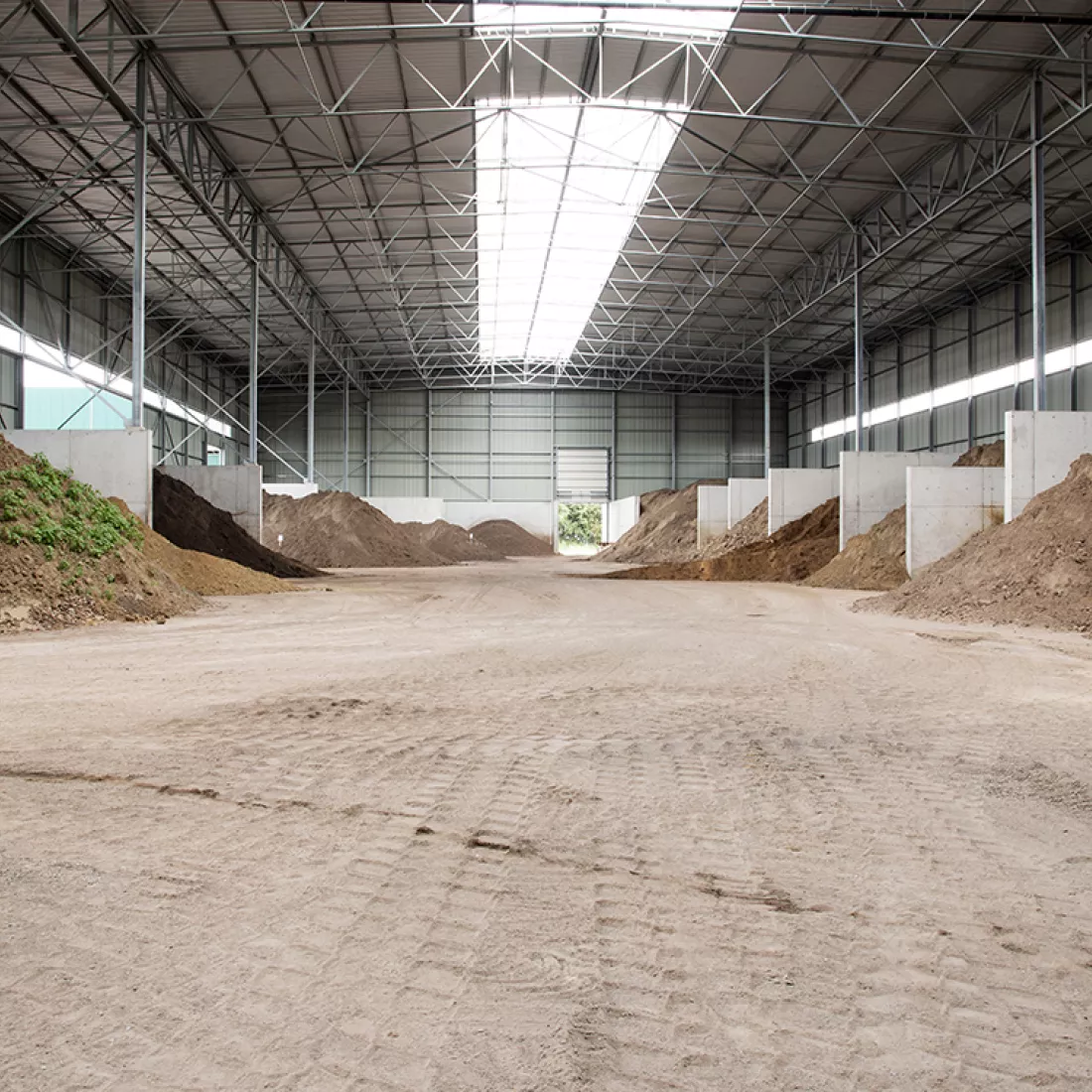 Binnenkant grondhal Rumst Recycling. Het zand ligt verdeeld in vakken. De vakken zijn duidelijk door betonnen muren. Het plafond bevat een grote lichtstraat.