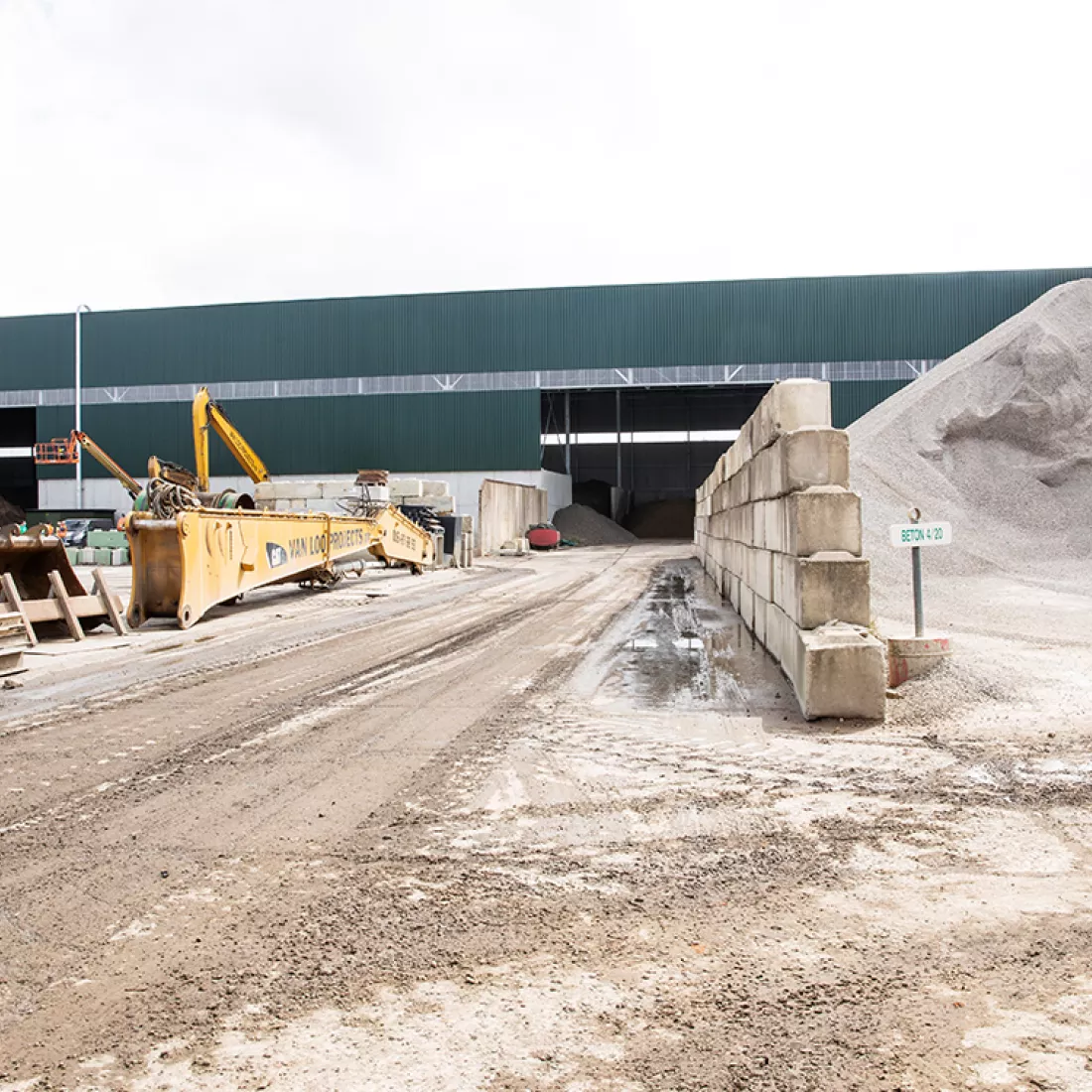 Grondhal Rumst Recycling. Achteraan bevindt zich de grondhal. Rechts ligt een soort zandberg en links werkapparatuur.