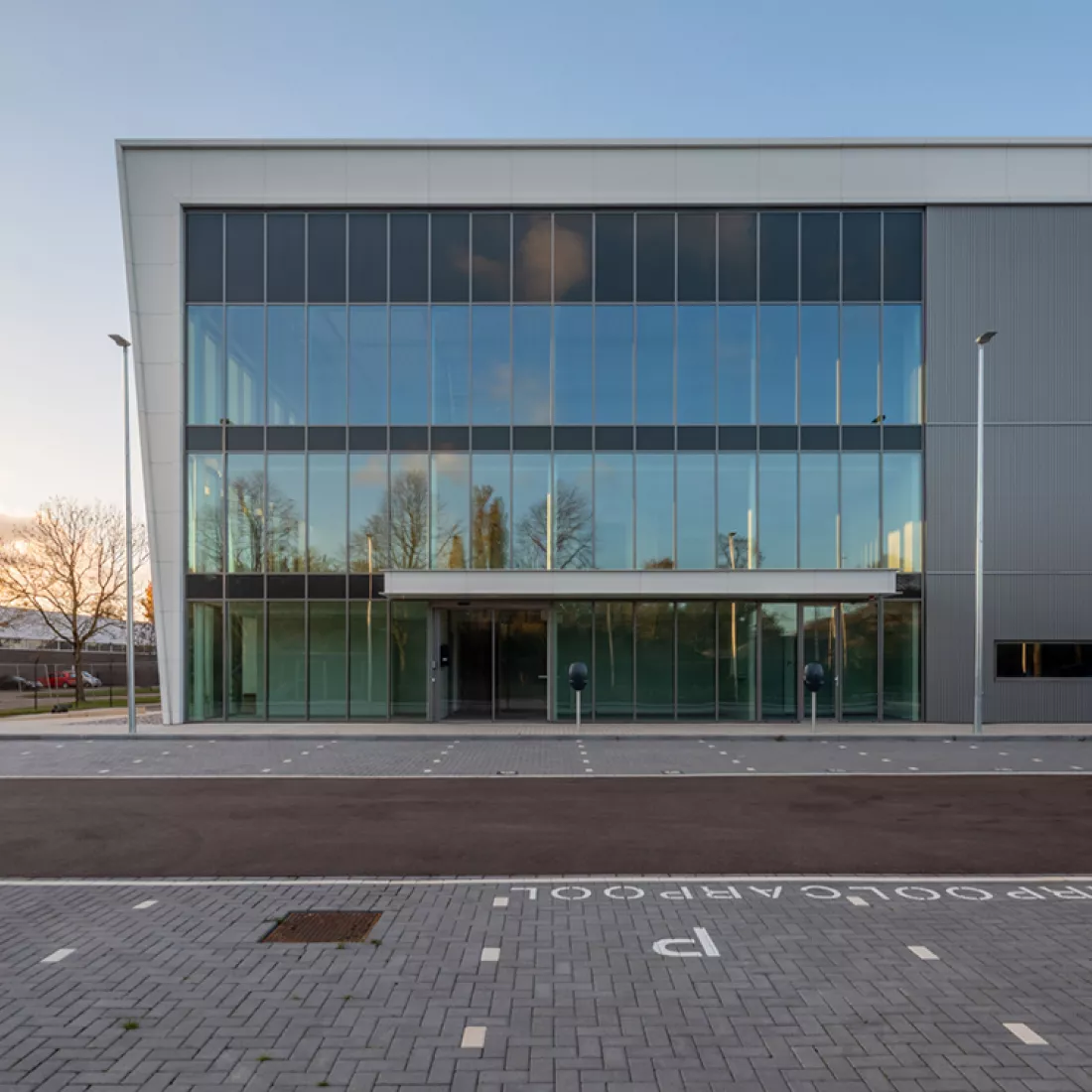Vooraanzicht kantoor - DC Braak. Het kantoor bestaat bijna volledig uit ramen. Voor het kantoor is er parking voorzien.