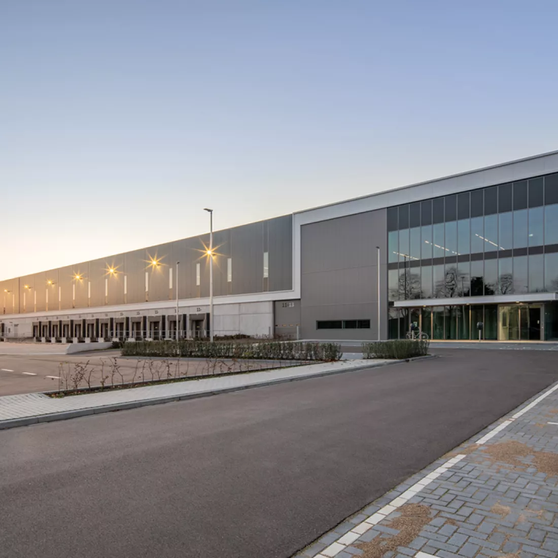 Zijaanzicht warehouse met kantoor - DC Braak. Rechts bevat het gebouw veel ramen. Links bevat het gebouw een dock voor vrachtwagens.