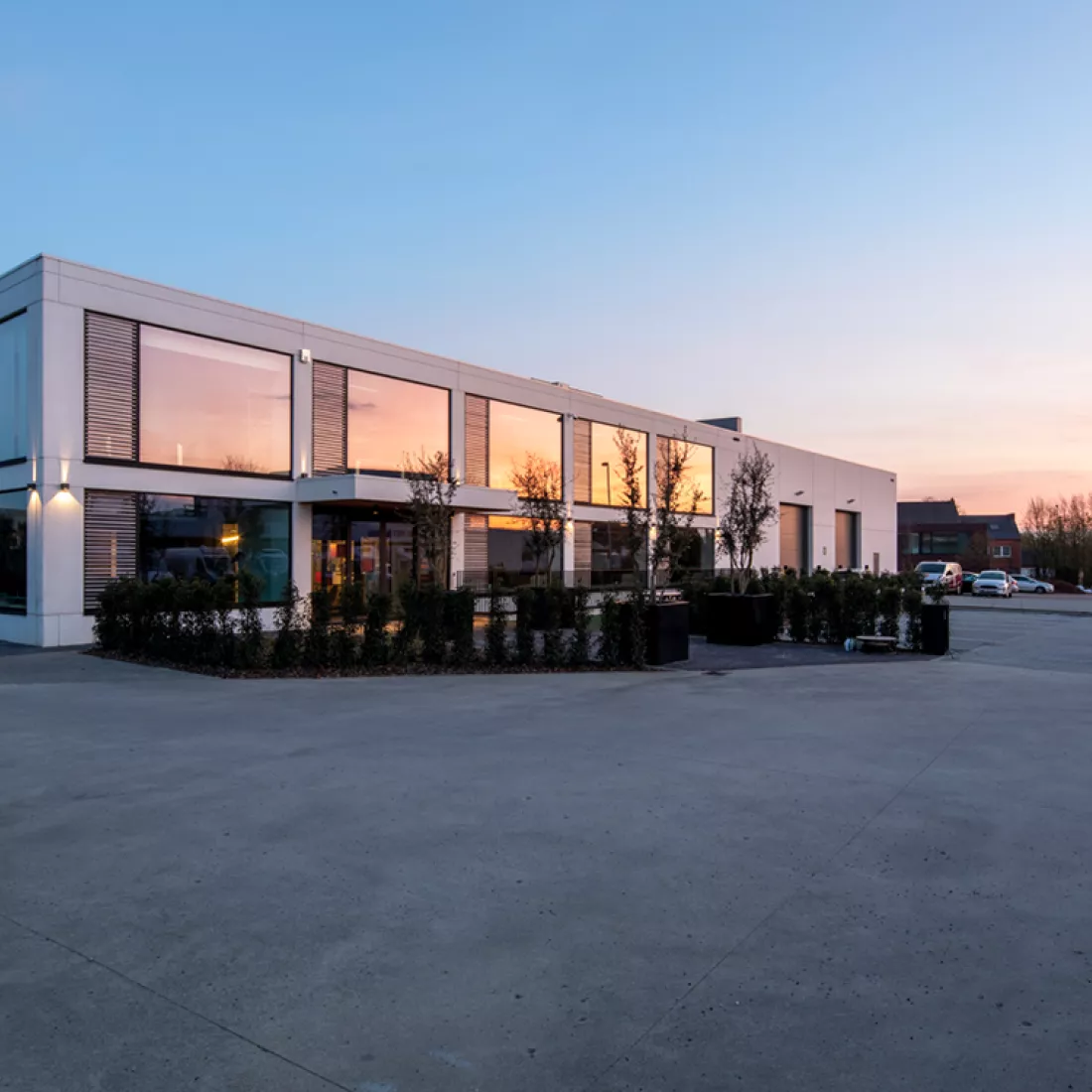 Zijaanzicht A & C Kantoor. Het gebouw is wit en bestaat uit twee verdiepen. Het kantoor heeft grote ramen met zwarte omranding. Ook zijn er zwarte poorten aanwezig. Het gebouw is gebouwd met staal.