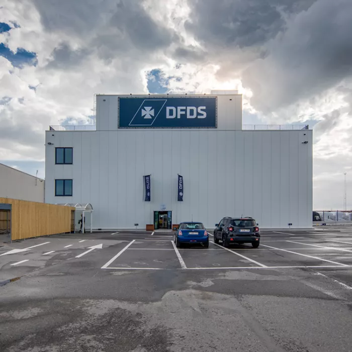 Vooraanzicht kantoor SEA Invest DFDS. Voor het kantoor zijn parkingplaatsen voorzien. Het gebouw is grijs en gemaakt uit staal.