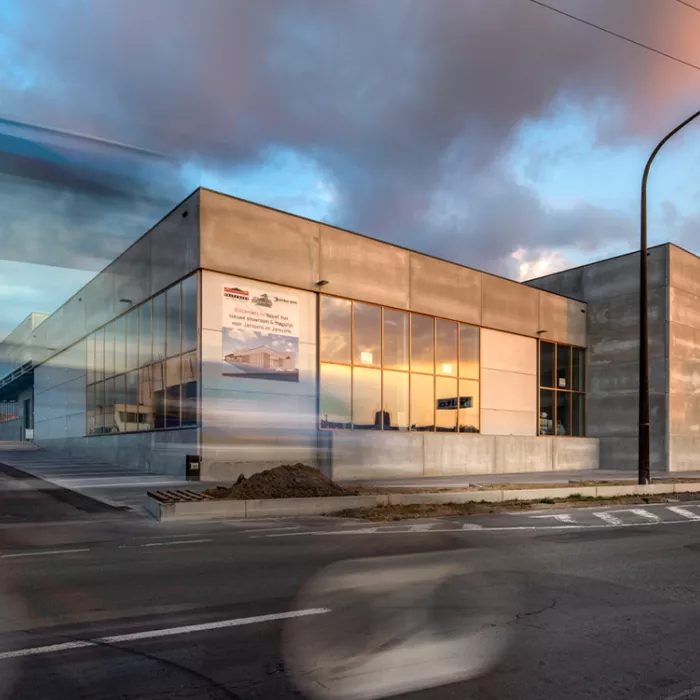 Zijaanzicht showroom Jofian. Het is een grijs gebouw met veel ramen. De afbeelding is gemaakt vanaf de overkant van de straat.