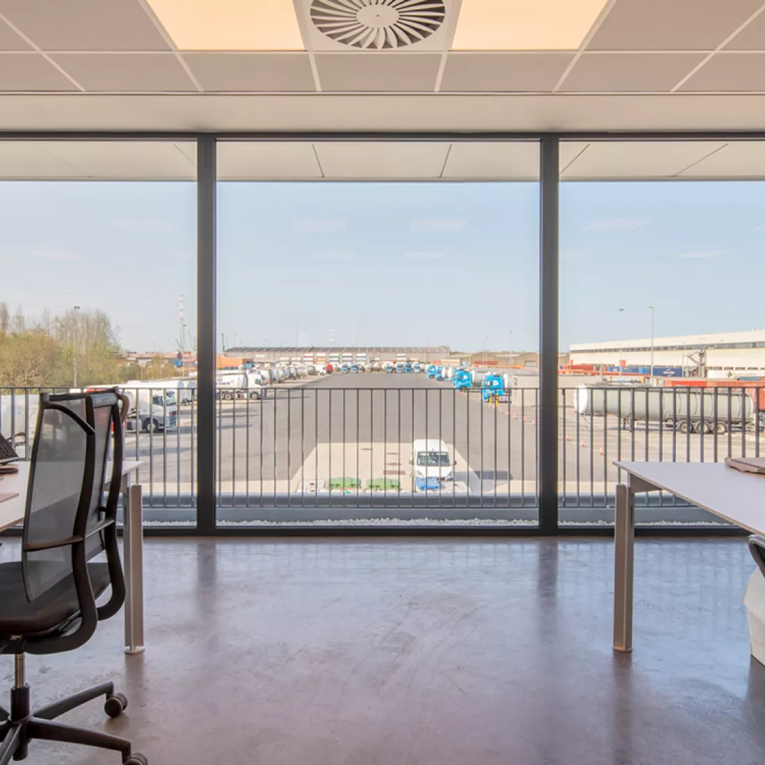 Binnenkant kantoor Thys Schenk. Zowel links als rechts bevinden zich bureaus. De muur bestaat uit ramen. Door het raam heb je zicht op de vrachtwagens.