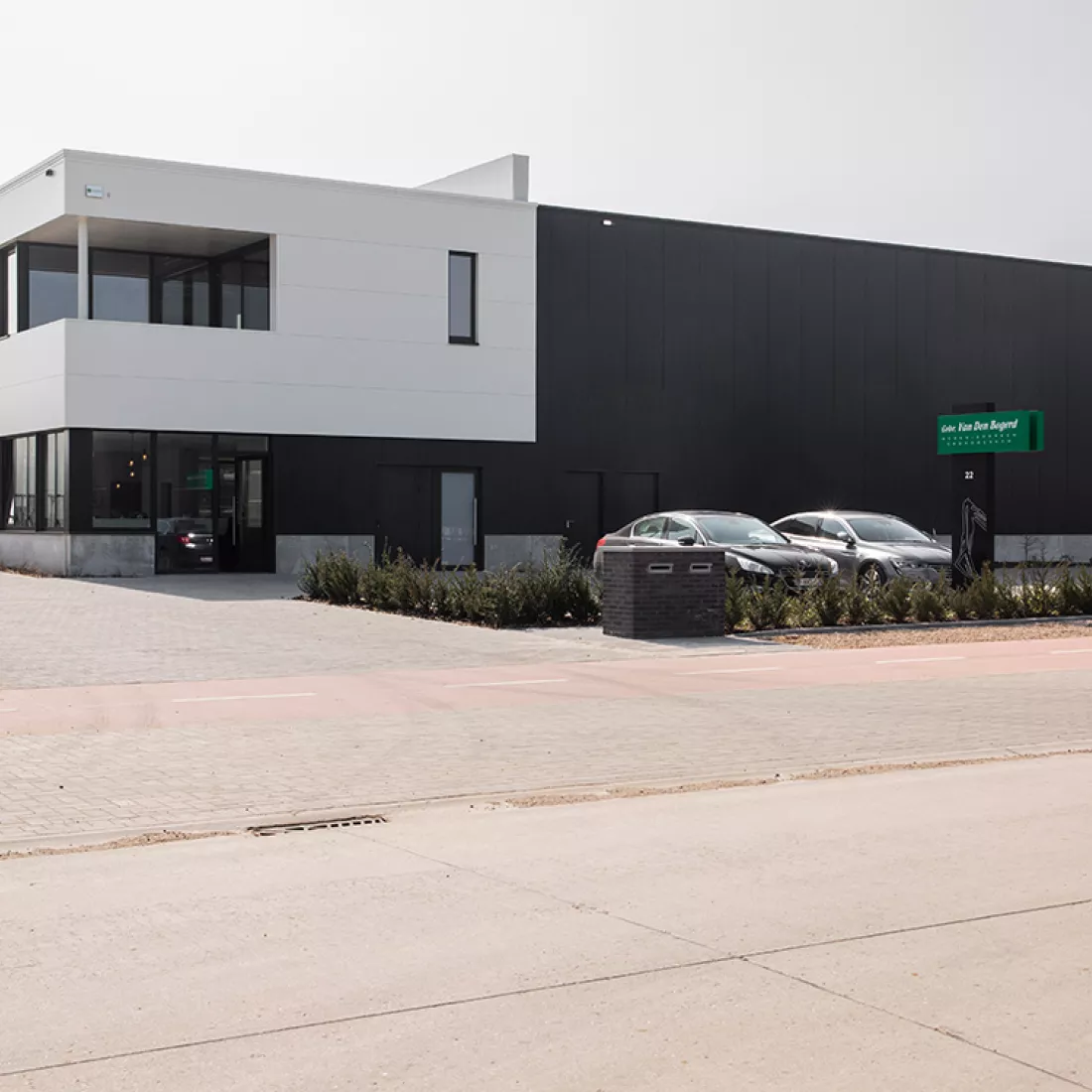 Vooraanzicht bedrijfsgebouw Van Den Bogerd. Het gebouw is zwart met wit. Voor het gebouw zijn parkeerplaatsen voorzien. Het gebouw is opgebouwd met staal.