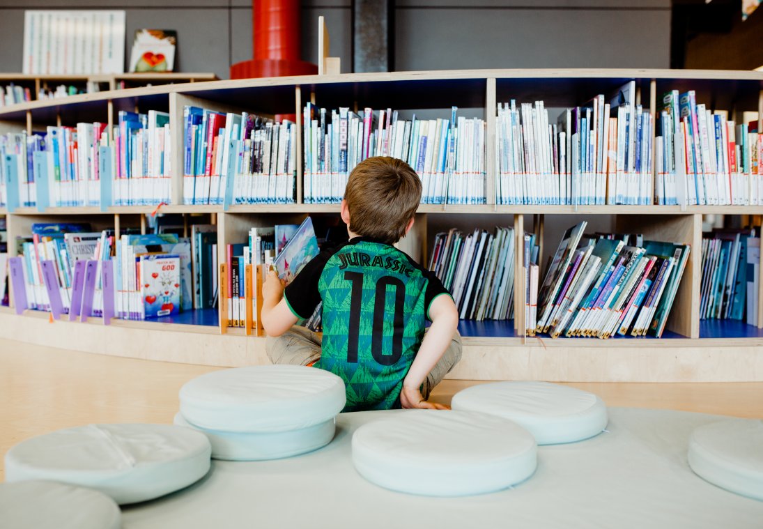 Kind zit voor boekenrek in de bibliotheek