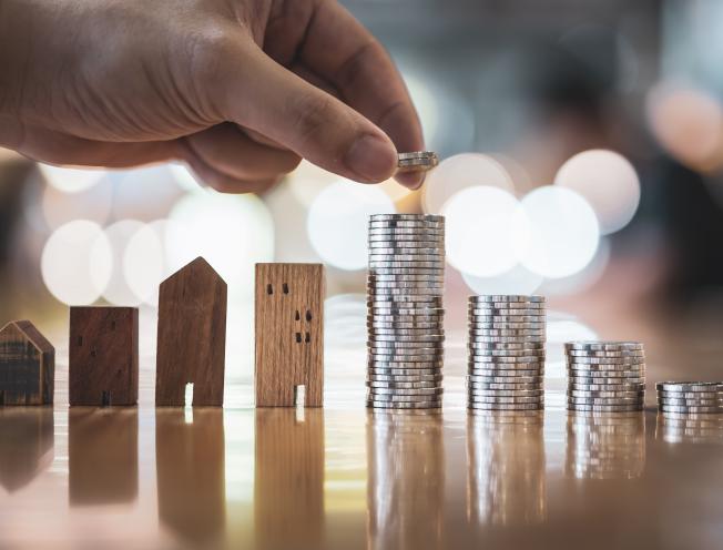 Hand choosing row of coin money on wood table and mini wood house (foto: Shutterstock, sommart sombutwanitkul)