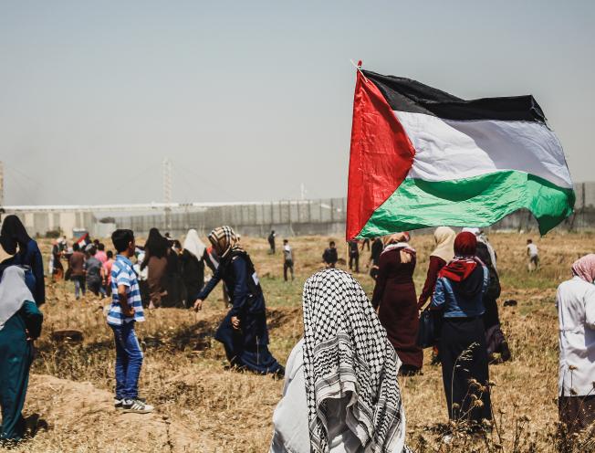 Persoon met Palestijnse vlag, in de verte is de afscheiding tussen Palestina en Israël zichtbaar