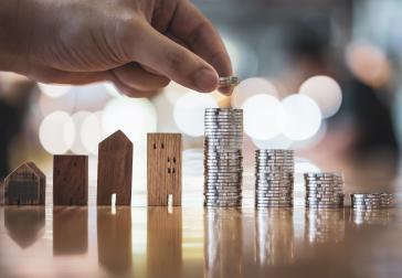Hand choosing row of coin money on wood table and mini wood house (foto: Shutterstock, sommart sombutwanitkul)