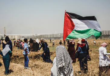 Persoon met Palestijnse vlag, in de verte is de afscheiding tussen Palestina en Israël zichtbaar