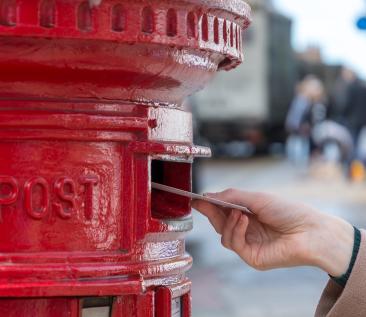 hand steekt brief in rode brievenbus