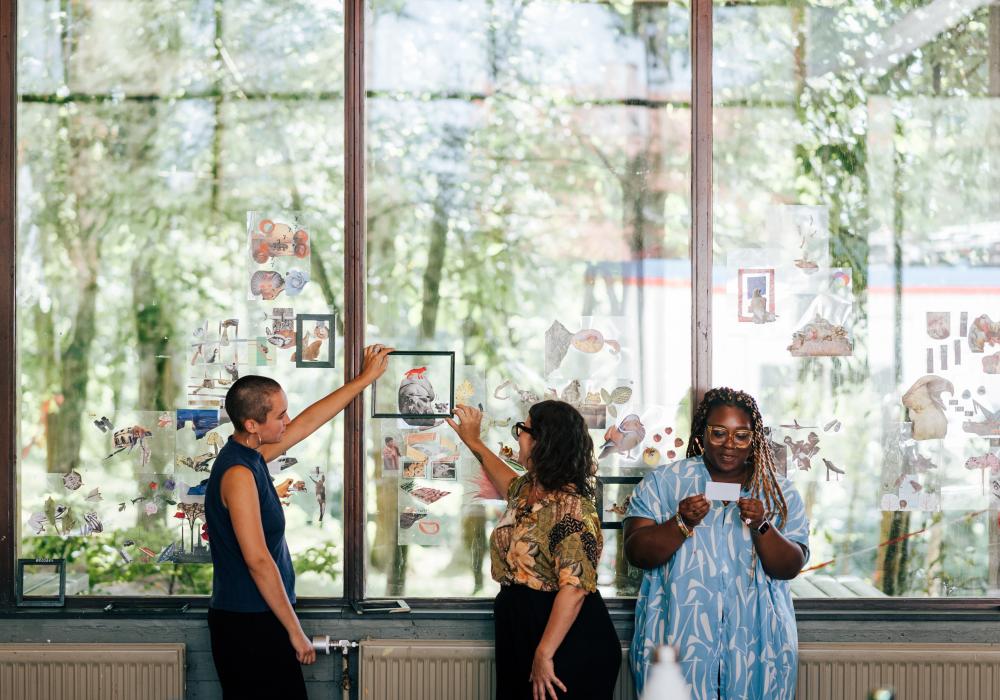 drie deelnemers staan voor een groot raam waar ze brainstormen rond beelden en collages