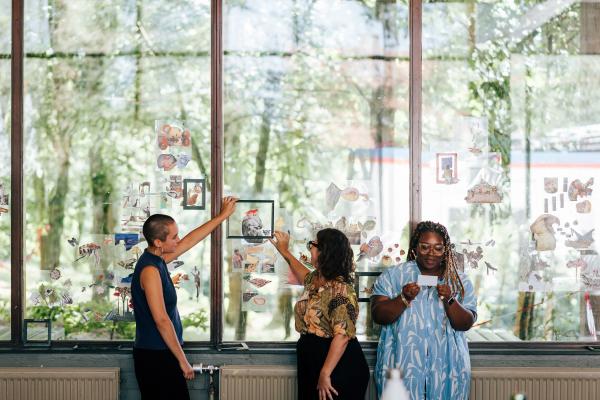 drie deelnemers staan voor een groot raam waar ze brainstormen rond beelden en collages