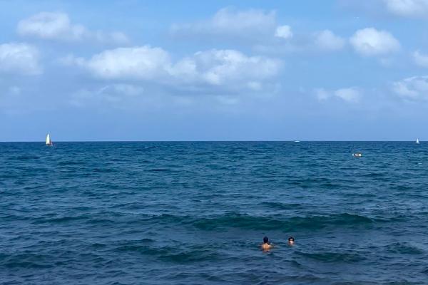 Foto van tijdens een DiscoverEU-reis: de zee, blauwe hemel met een paar wolkjes, twee jongeren zwemmen in de zee